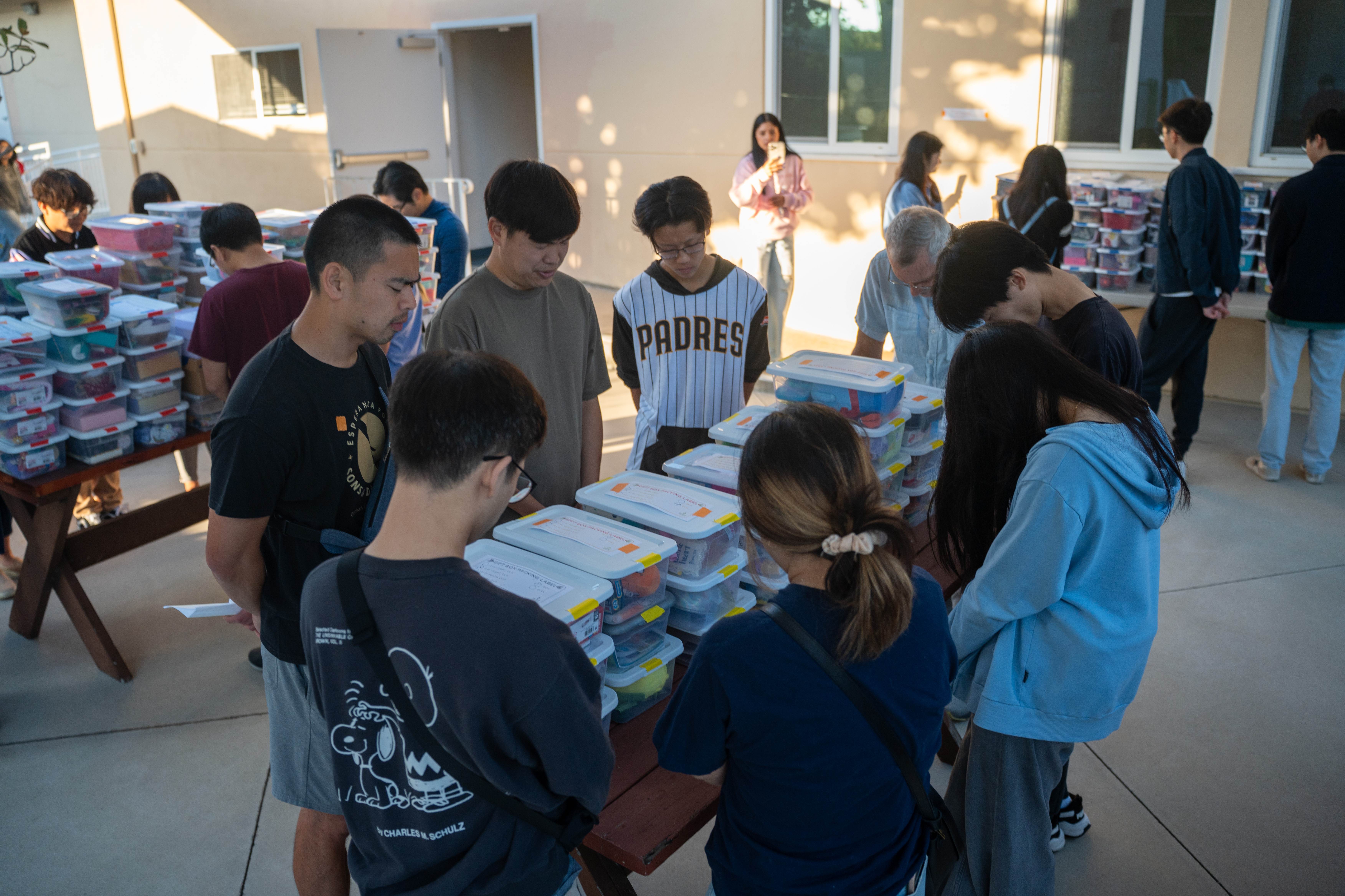 Renewal Missions volunteers bowing their heads in prayer around a table of Christmas gift bins on Packing Day